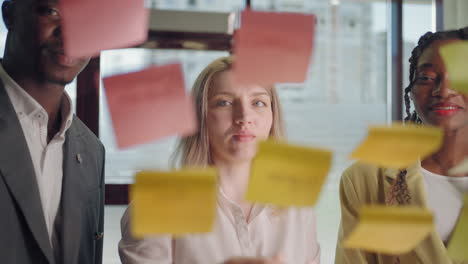 multiracial team van kantoorwerkers bespreken project kleven stickers op glazen muur brainstorm en nieuw idee