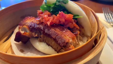 Delicious-hot-steam-bao-bun-with-pork,-coriander-and-sweet-onions,-traditional-Asian-food-at-a-restaurant,-4K-shot