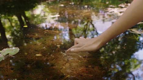 woman hand touching water in pond with finger making ripple