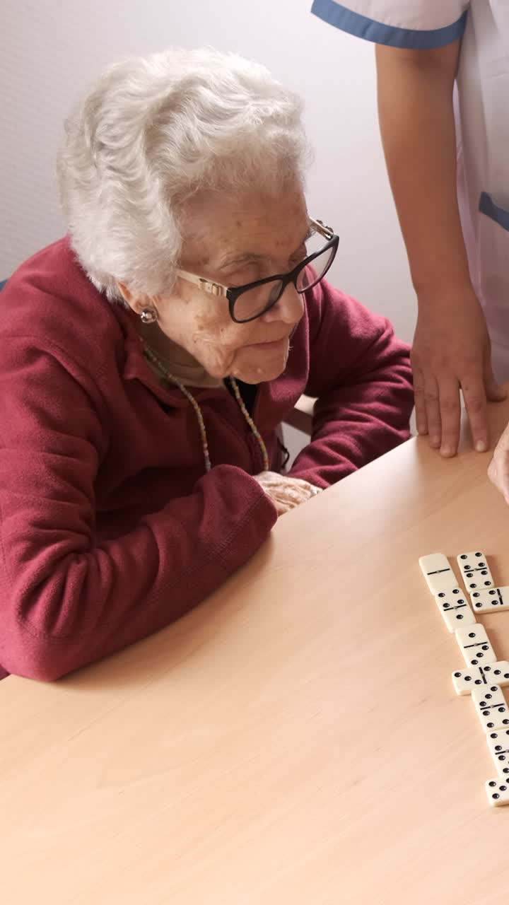Nurse playing dominoes with senior man and woman in canteen of nursing home