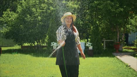 woman watering garden plants with hose in sunny backyard surrounded by lush greenery