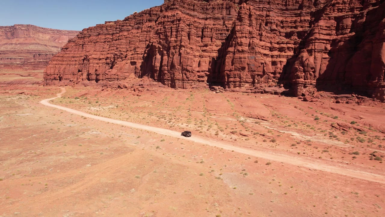 Drone che vola lateralmente filmando un'auto 4x4 che guida su una strada sterrata tra le montagne di roccia rossa di Moab, USA in 4k.