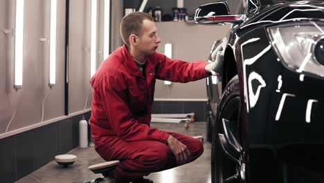 trabajador de autocentro haciendo la limpieza final de un coche negro nuevo y perfectamente pulido.