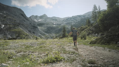 Hiker-walking-in-the-valley-with-hiking-poles-surrounded-with-mountains-on-a-sunny-sumer-day