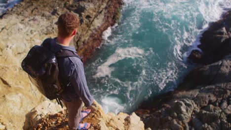 High-angle-view-of-a-man-looking-down-at-the-ocean-from-the-edge-of-a-sea-cliff