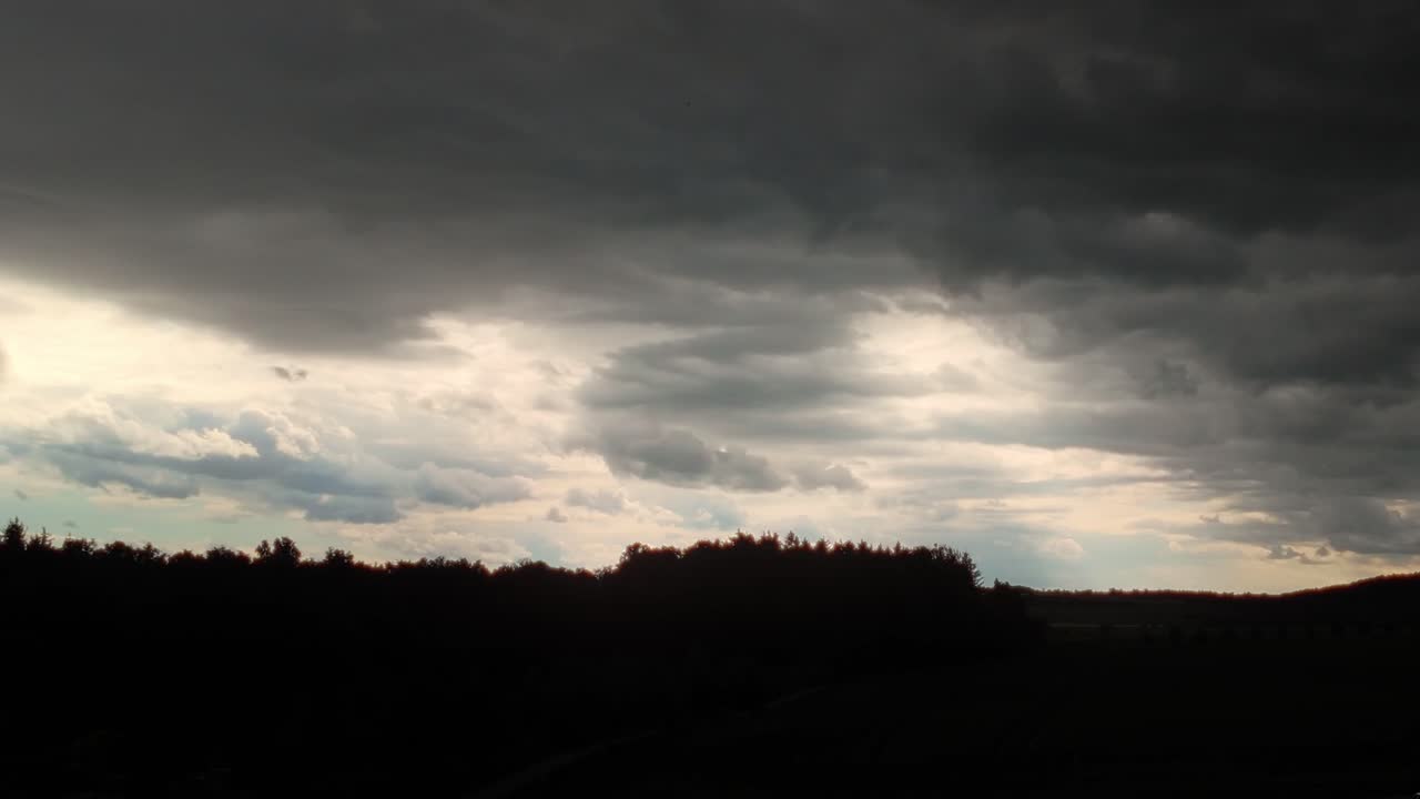 Timelapse of dramatic clouds with sun rays shining through. Silhouette of swaying trees below. Spectacular scenery