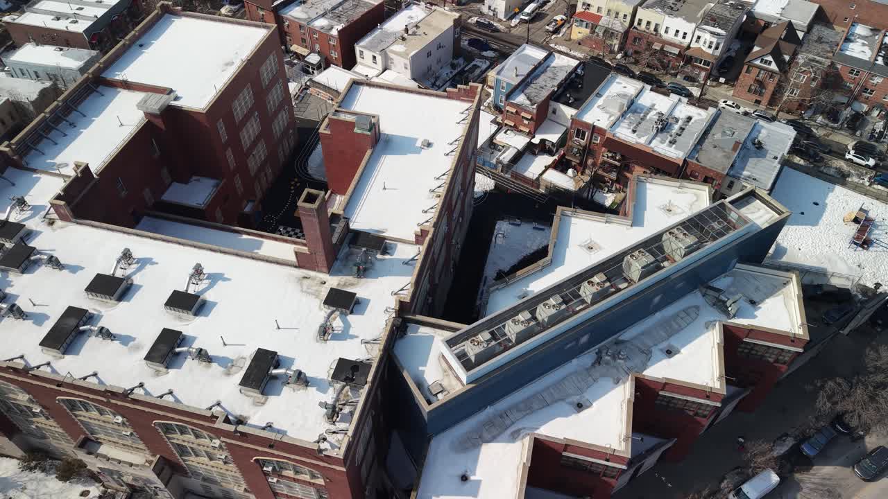 High angle aerial perspective slowly rotating above a dense urban neighborhood with residential buildings, streets, and cars, featuring rooftops and courtyards covered with fresh white snow