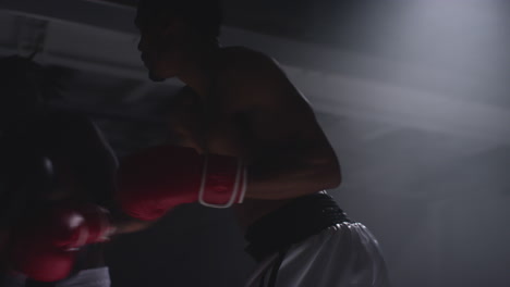 toma de cerca de dos boxeadores masculinos con guantes en el ring de boxeo luchando en un partido de boxes con iluminación de baja clave