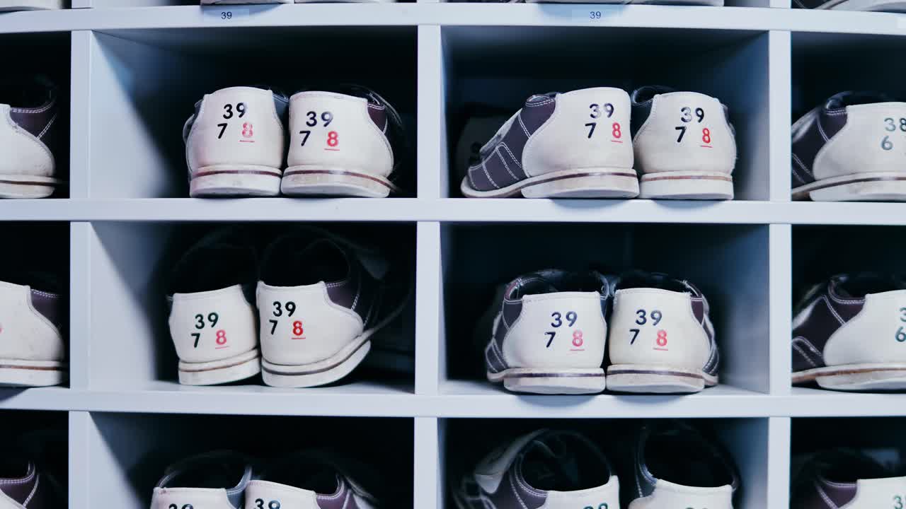 Organized rows of bowling shoes as person selects a pair by hand indoors