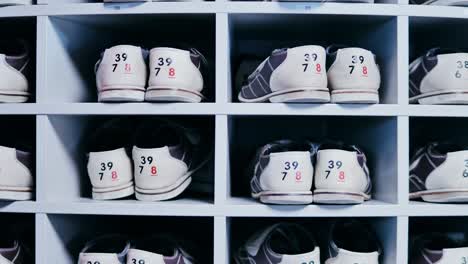 organized rows of bowling shoes as person selects a pair by hand indoors