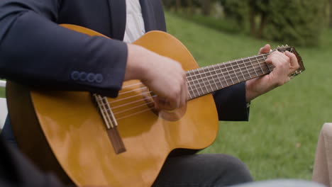 irreconocible hombre de mediana edad chapando una guitarra sentado en la mesa con sus amigos durante una fiesta al aire libre en el parque