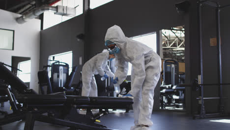 team of health workers wearing protective clothes cleaning gym by using disinfectant sprayer