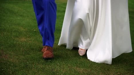 closeup shot of the legs of bride and groom walking together on the grass in the park on the sunny wedding day