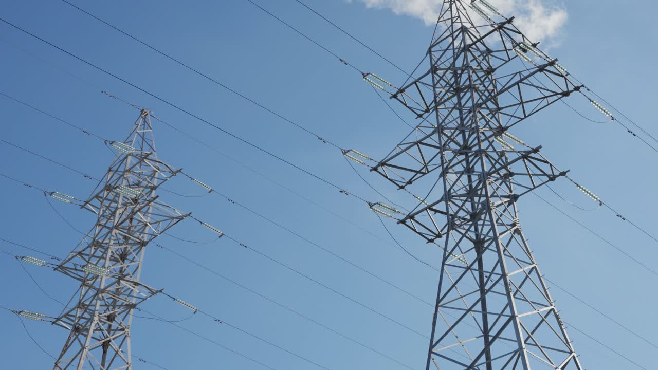 High-voltage power transmission towers and cables stretch across a clear blue sky, symbolizing energy infrastructure, connectivity, and industrial engineering