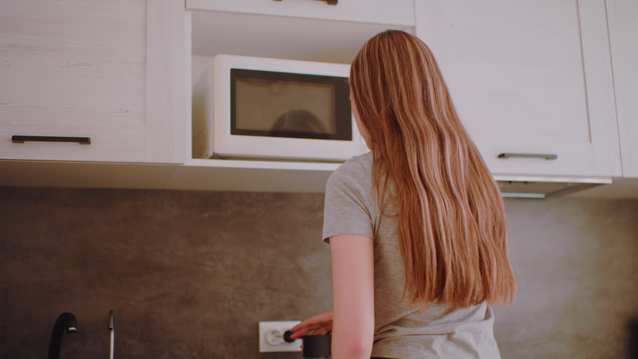 Independent woman in kitchen reaches upper cabinet to take coffee container, lowers it to counter preparing for morning drink, ready to bring cup and spoon under soft