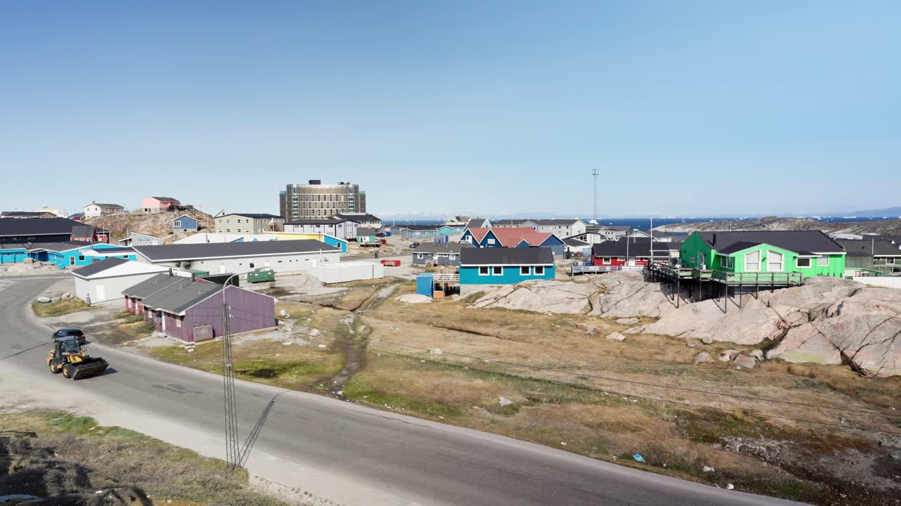 A vehicle drives down a street in Ilulissat, Greenland. The town's iconic colorful houses line the road, illustrating daily life and transportation in a remote Arctic community