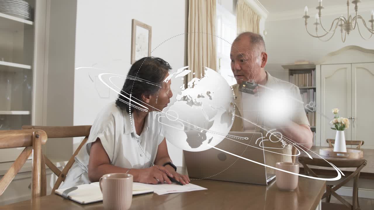 Mature man placing laptop and senior woman marking papers in dining, globe orbiting finance data