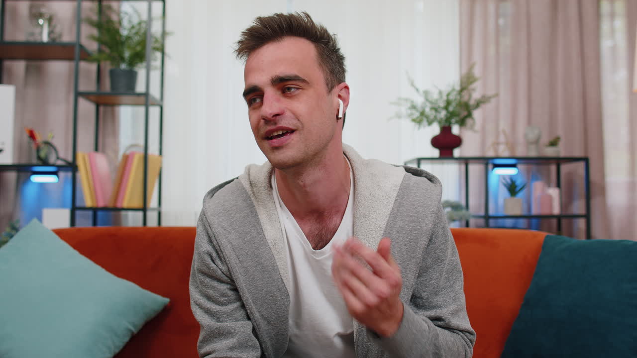 Uomo seduto sul divano di casa, che guarda la telecamera, in videochiamata con amici o genitori.