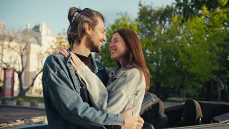 young brunette girl hugging her brunette boyfriend near their cabriolet on a sunny summer day. happy life in the city