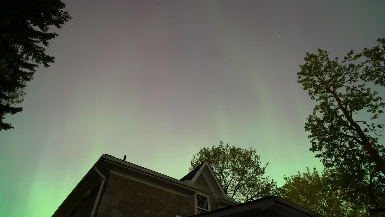 aurora boreal bailando sobre una casa y árboles, time-lapse