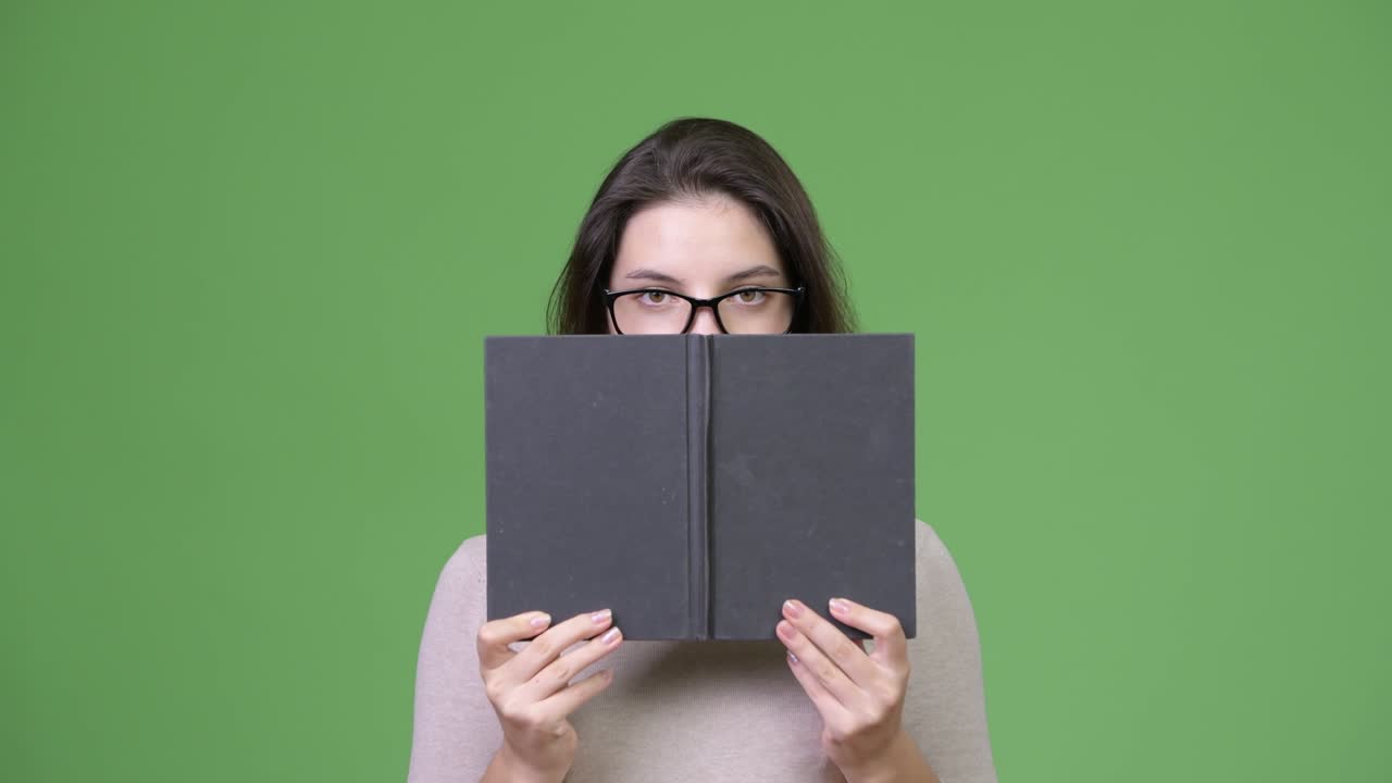 Young beautiful woman hiding behind book