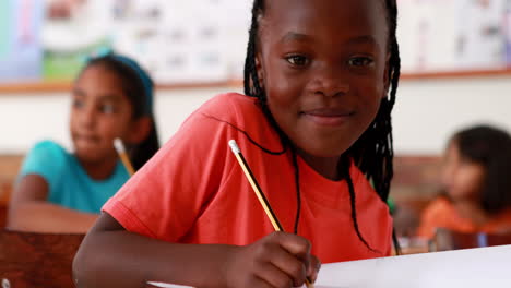 little girl writing and smiling at camera during class