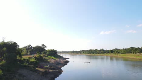 Aerial-footage-of-a-small-wooden-boat-on-a-large-Asian-river,-a-tranquil-and-idyllic-scene