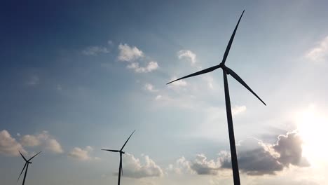 Three-windturbines-spinning-in-silhouettes-in-the-afternoon-while-clouds-are-moving-towards-the-horizon-and-the-sky-is-blue