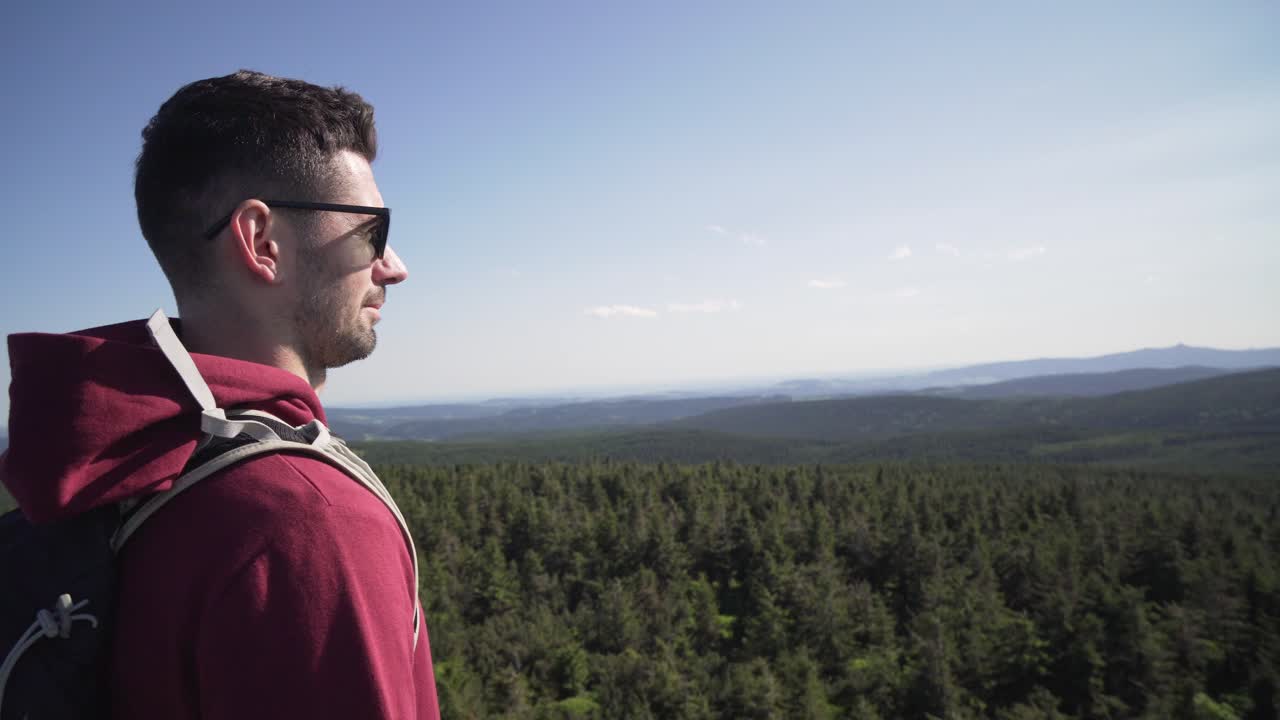 Young tourist man standing at the top of hill, relaxing and looking around, side shot