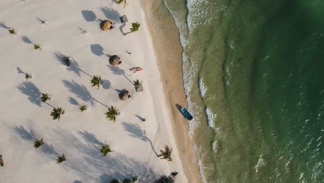 Schöne-Lange-Schatten-Von-Den-Hohen-Grünen-Palmen-über-Dem-Weißen-Sandstrand,-Während-Die-Wellen-Sanft-Auf-Den-Strand-Rollen,-Wo-Ein-Blaues-Boot-Festgemacht-Ist