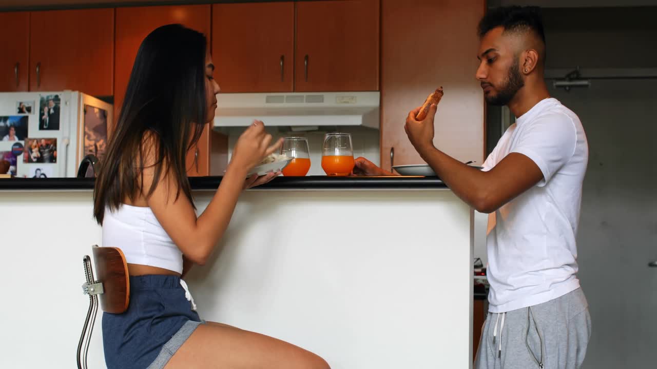 vista lateral de una joven pareja asiática comiendo juntos en la cocina de casa 4k