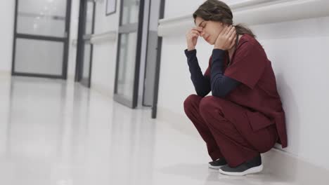 tired caucasian female doctor squatting in hospital corridor, slow motion