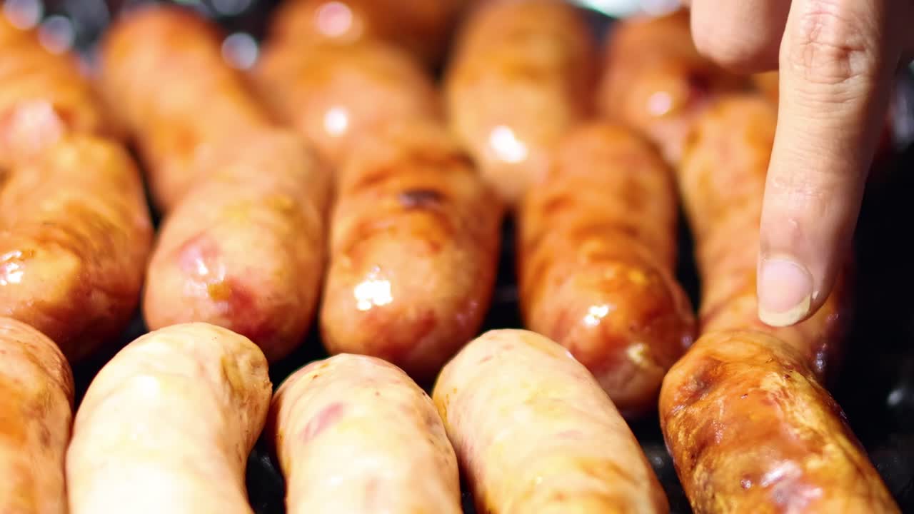 A detailed view of sausages being turned on a grill using tongs, highlighting their browning and texture.