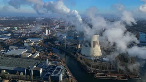 aerial view of a thermal power plant emitting smoke on a sunny day, with a river and a city in the background. fabulous aerial view flight drone camera pointing down