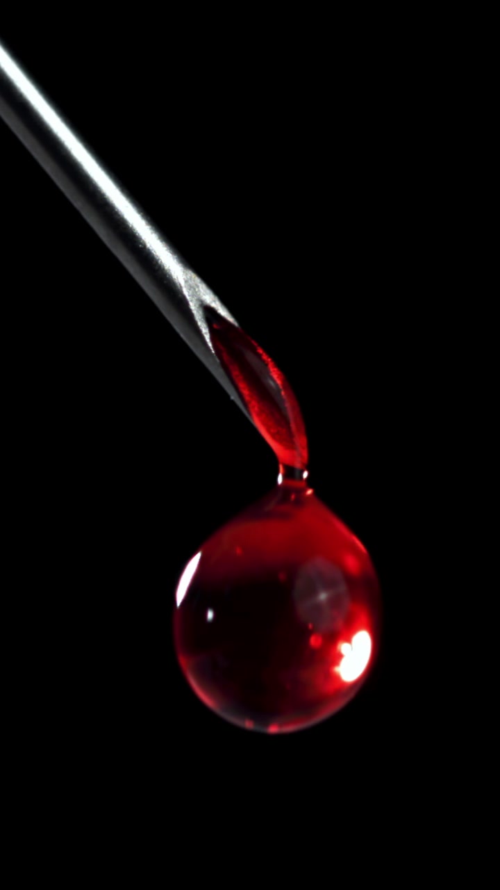 Roter Blutstropfen tropft von der Spitze einer medizinischen Nadel