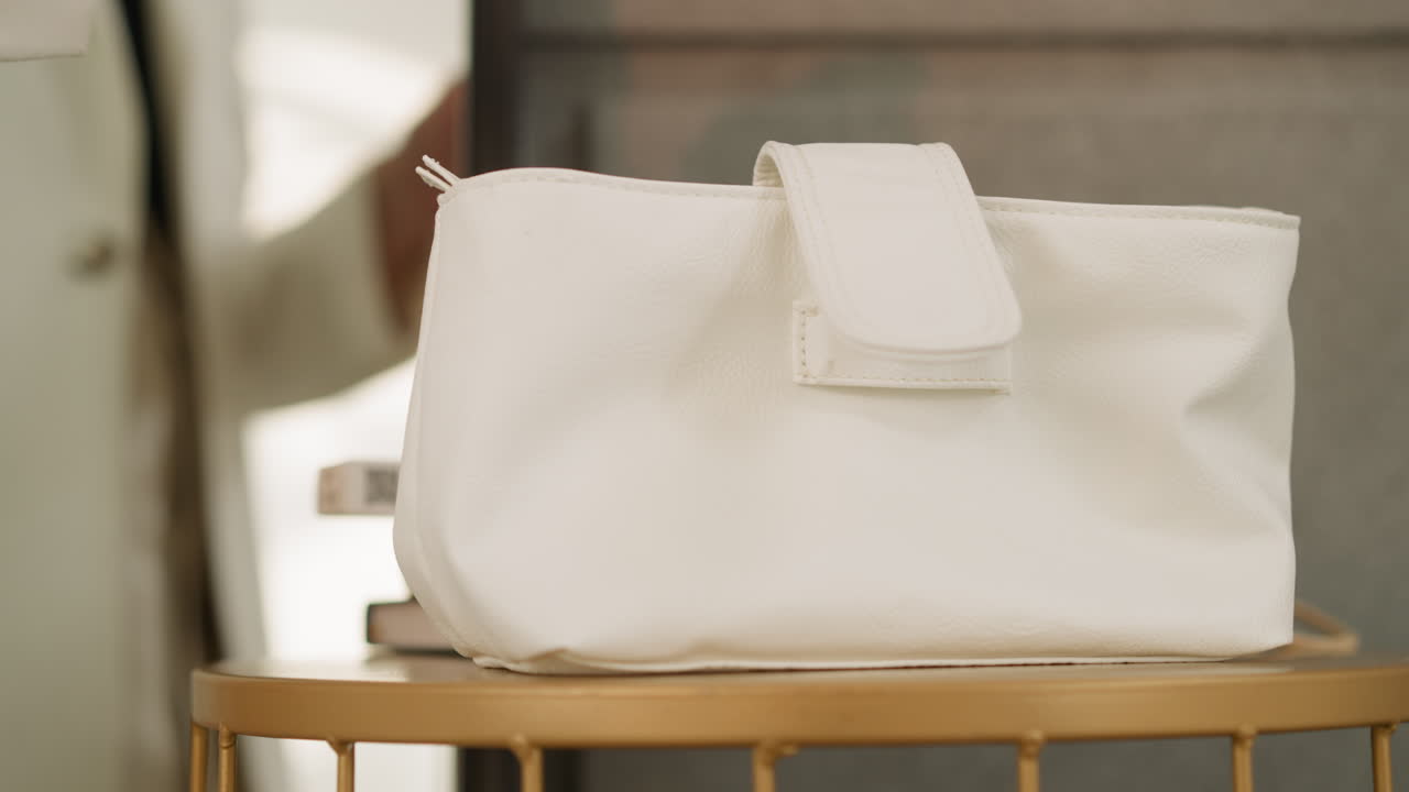 Mano di donna con manicure curata che appoggia una borsa bianca sul tavolo.