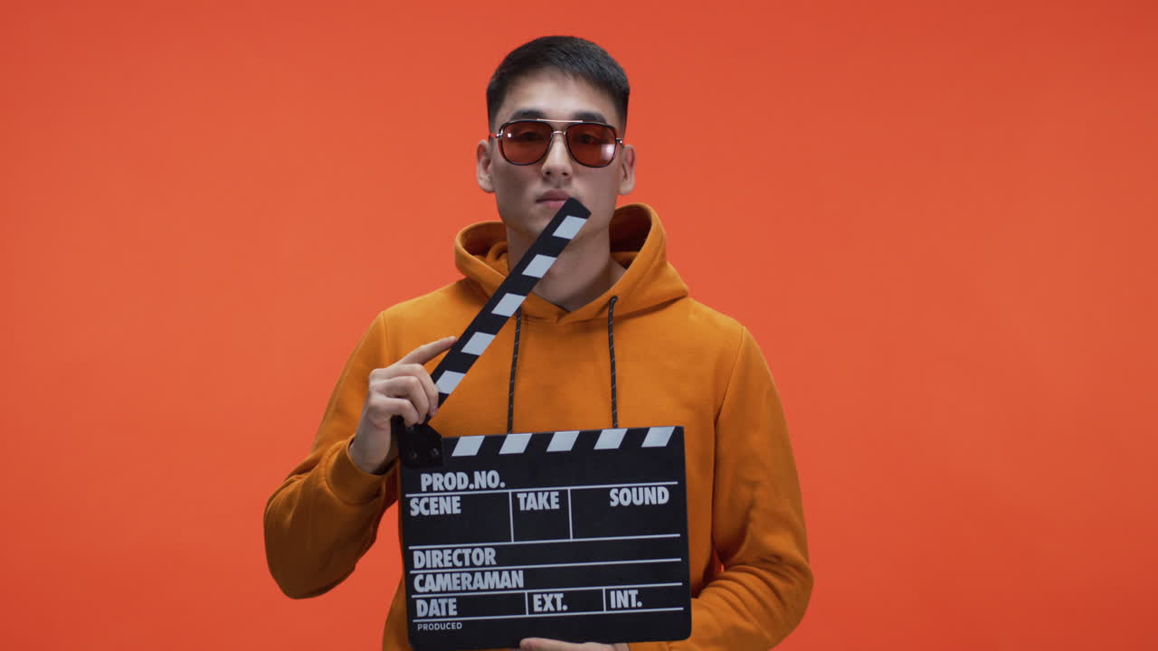 Man Holding Clapperboard in Front of Orange Background