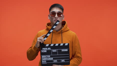 man holding clapperboard in front of orange background
