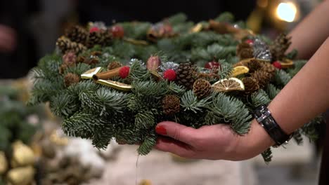 person holding beautiful and colourful hand made christmas wreath, green spruce branches decorated with pine cones and other decorations. christmas chaplet in hands.