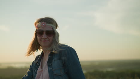 una mujer despreocupada con una cinta floral en la cabeza y gafas de sol baila de alegría, sonriendo y levantando las manos
