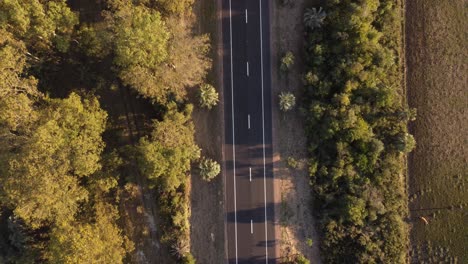 aerial top down ascending view over car driving along straight rural country road of uruguay