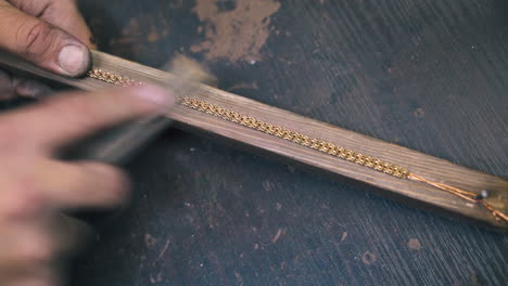 jeweler-grinds-golden-bracelet-on-wooden-gutter-close-view