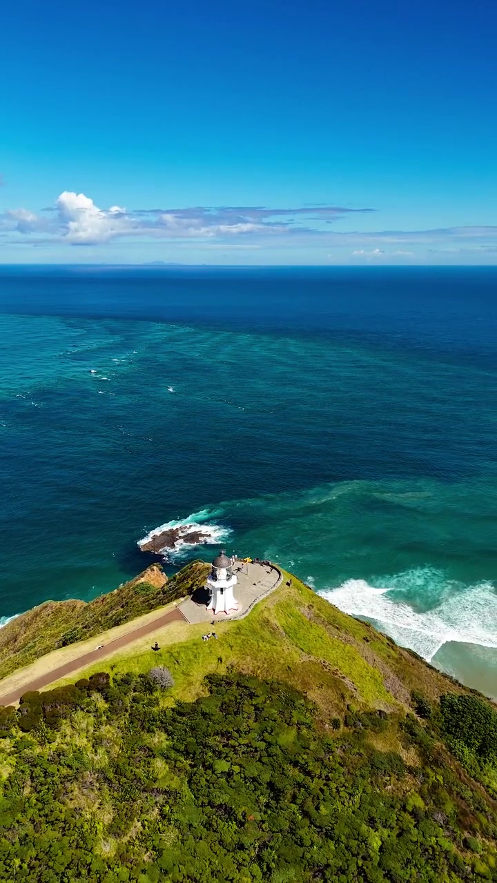 Faro di Cape Reinga sulla costa settentrionale della Nuova Zelanda che si affaccia su scogliere aspre, acque marine turchesi e potenti onde oceaniche. Ideale per progetti di viaggio e natura, vista aerea verticale.