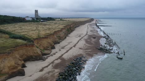 slow moving aerial footage along the tide coming in onto sea defences towards church