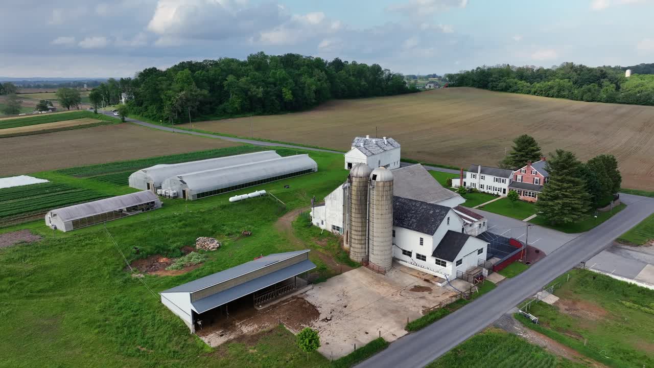 Aerial rising shot of american farmers house with silo storage and barn. Quiet rural suburb district of american town. Backwards shot. Spring day with intersection road and forest Trees.