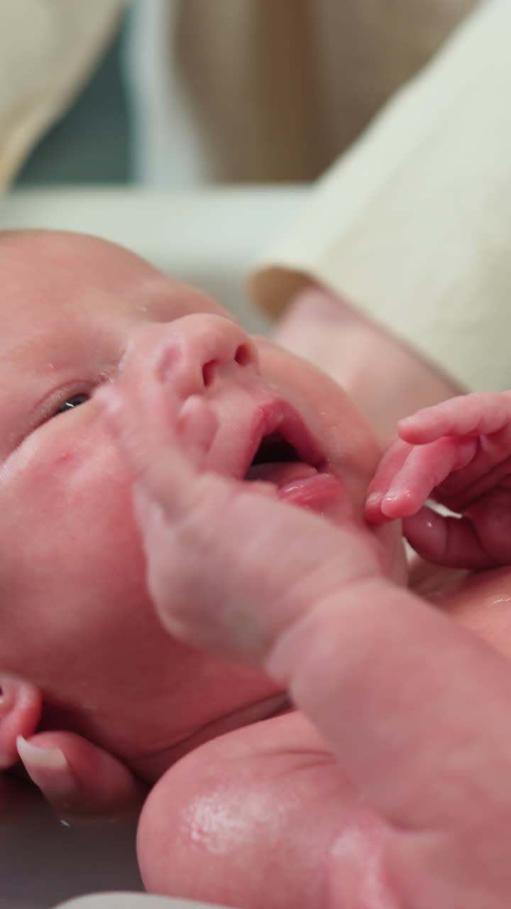 Primer plano del rostro de un bebé recién nacido al que se le lava suavemente durante el baño con agua y jabón suave.