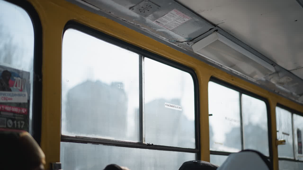 window view inside moving train with heads of seated passengers in winter light, smudged glass and yellow frames sliding past city scenery, gentle motion and reflections across panes