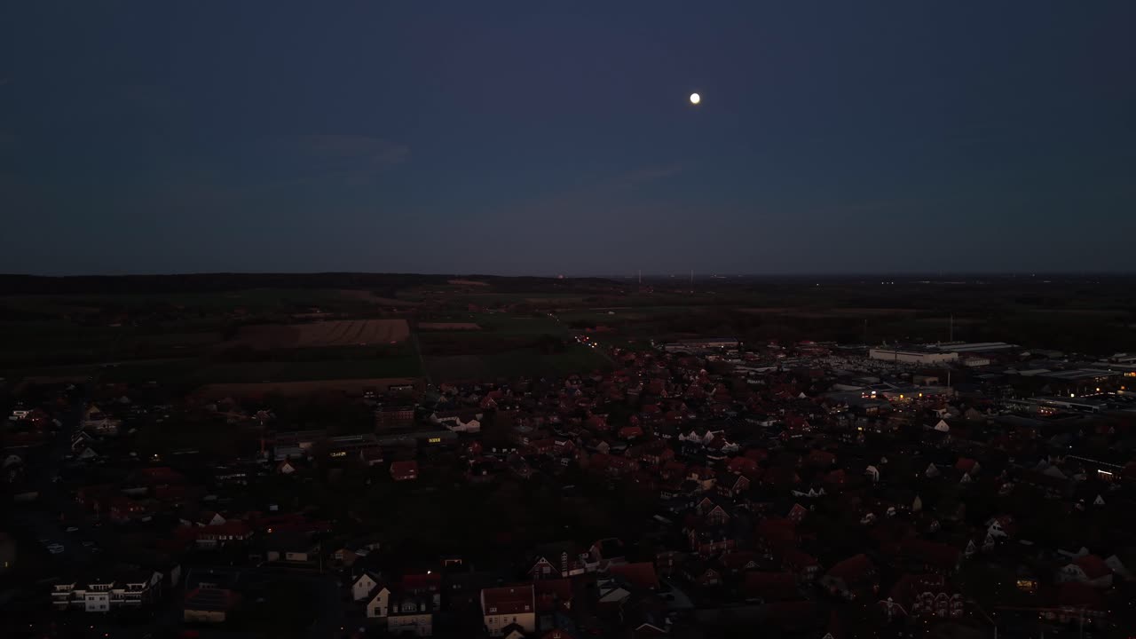 Vista aerea al crepuscolo di una città tedesca con fitti tetti di mattoni rossi e la campagna circostante sotto una luminosa luna piena che sorge nel cielo serale. Veduta panoramica. Tranquillo quartiere residenziale in primavera