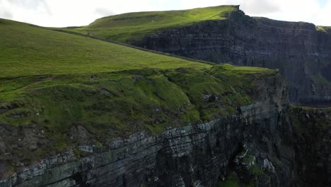 Person-hiking-along-Cliffs-of-Moher-Atlantic-Ocean-walk,-aerial-forward-dolly