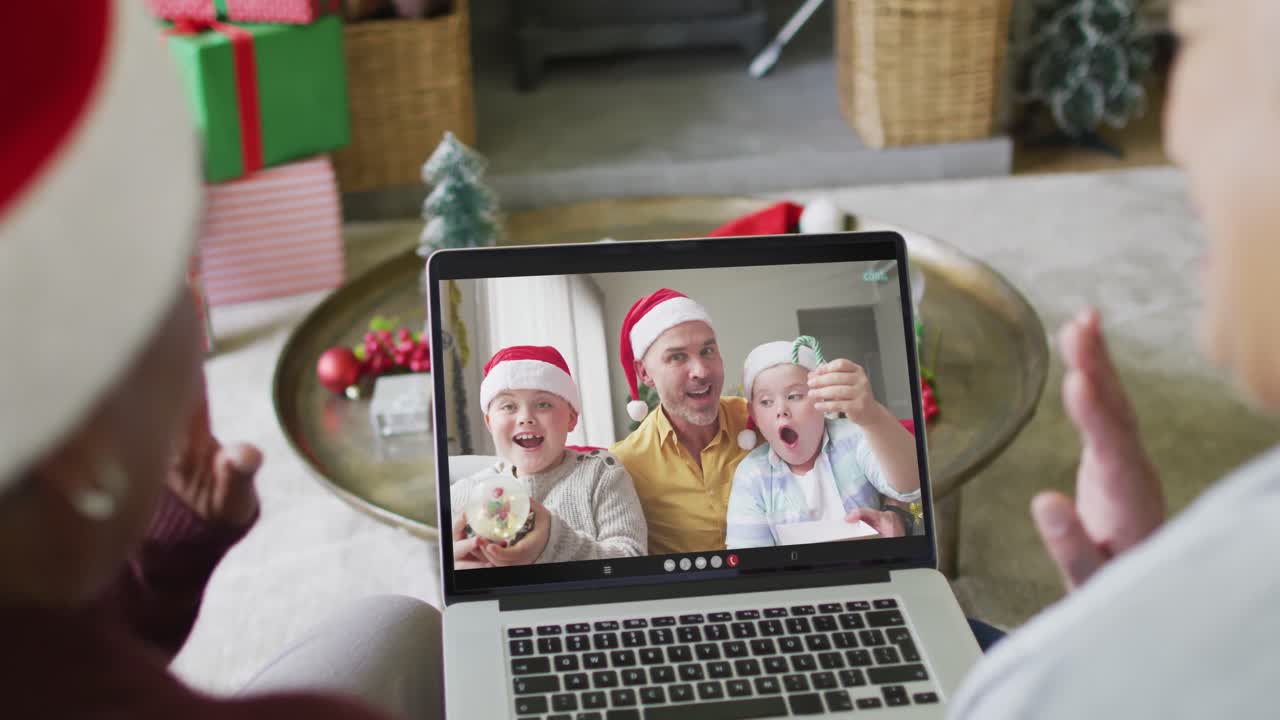 diversas amigas mayores que usan una computadora portátil para una videollamada de navidad con una familia sonriente en la pantalla
